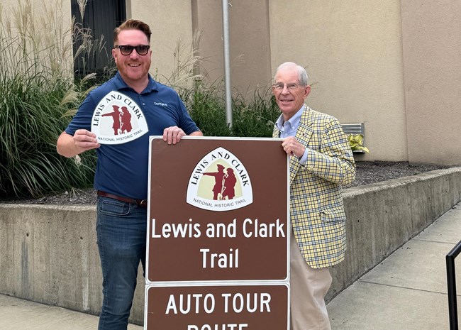 two men stand with a road sign