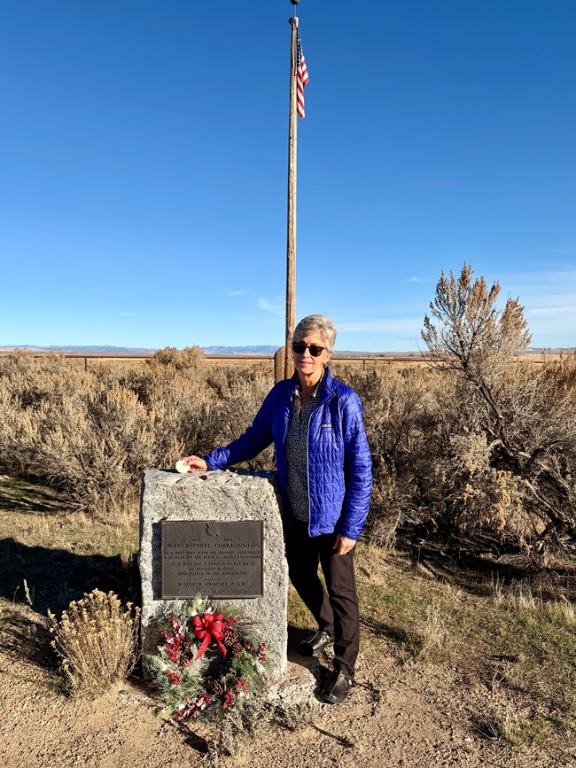 a woman stands next to a stone and commemorative plaque in front of the American flag