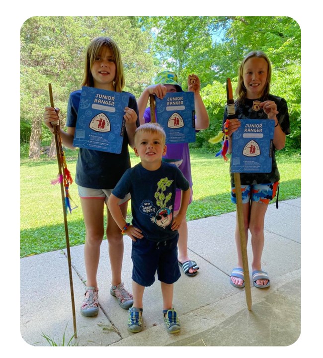 Four children pose with blue booklets and badges. Boy in front smiles broadly with hands on hips.