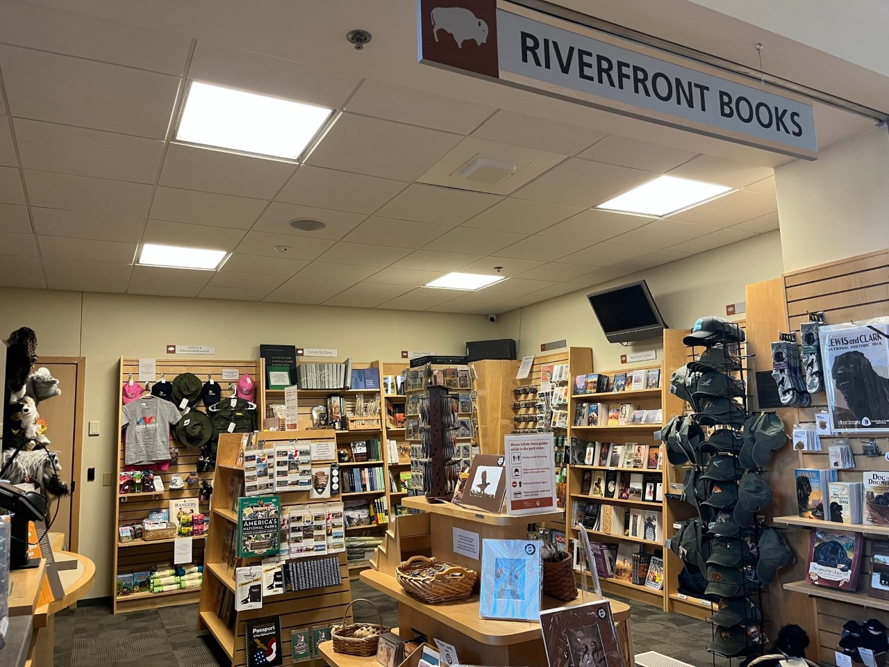 Small bookstore. Sign reads Riverfront books. Racks ine walls with books, tshirts, and memorabilia.