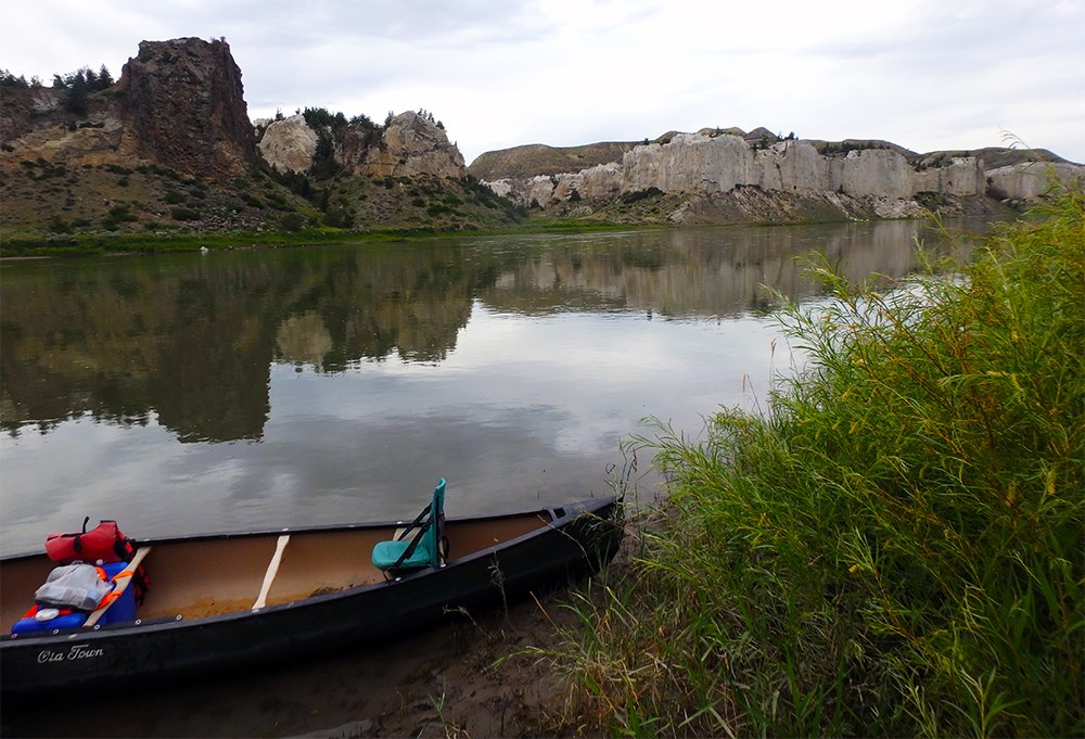 Canoe on the shore of a river. Sandstone cliffs in the distance.