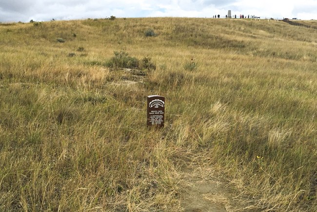brick red headstone marker in grassy field with text: Wasicu Sapa Black White Man A Minnikojou Lakota Warrior fell here on June 25 1876 while defending the Lakota way of life