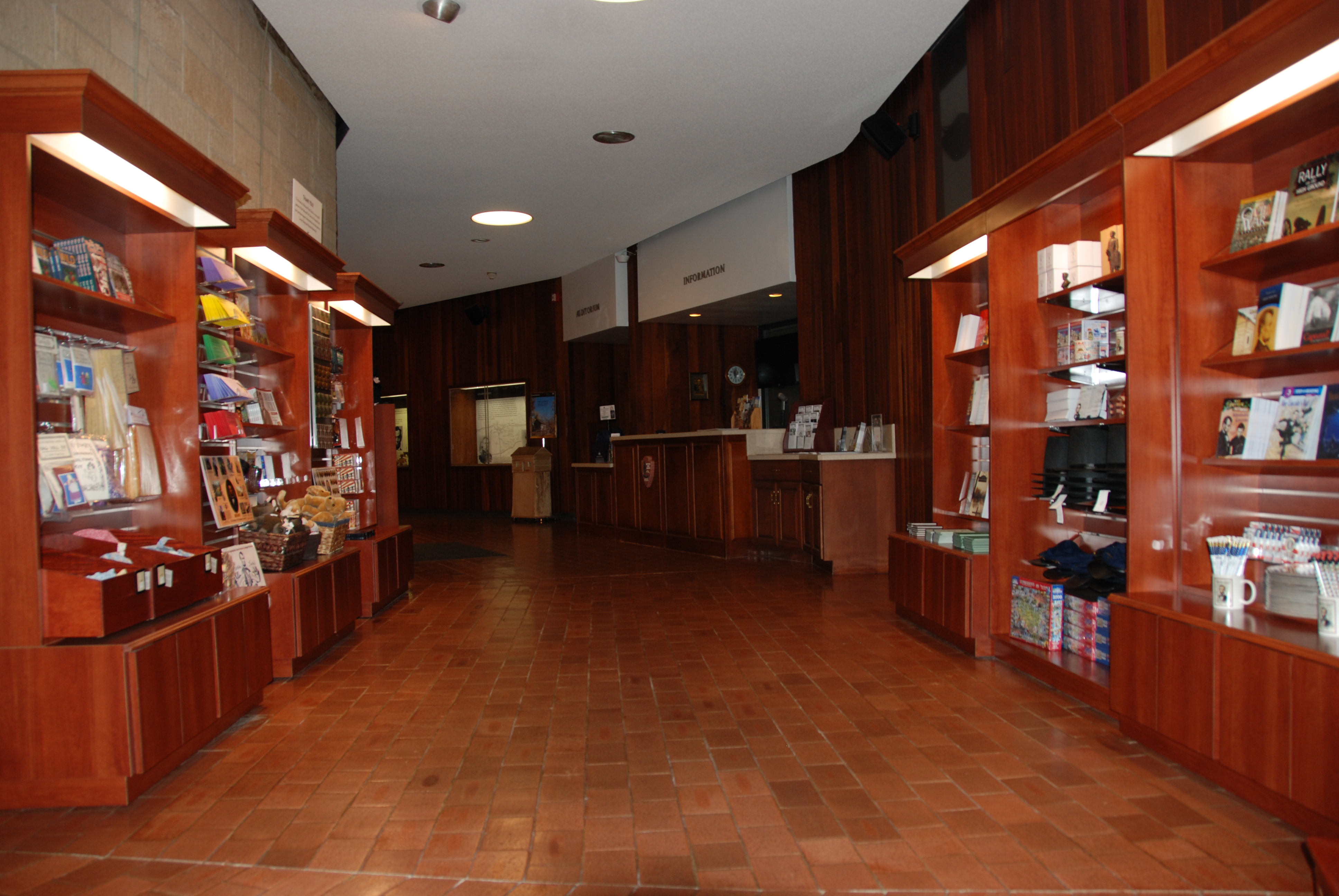 Six bookshelves on both sides of aisle filled with books, games, toys, and other sale items. Information desk and entrance to auditorium in back.