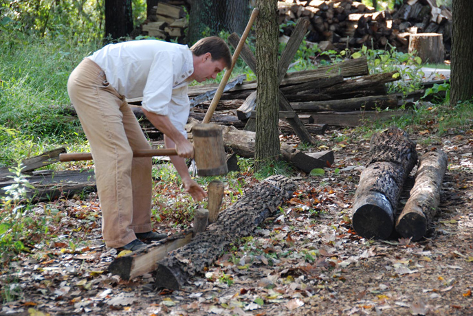 Park Ranger in 1820s period clothing splitting rails.