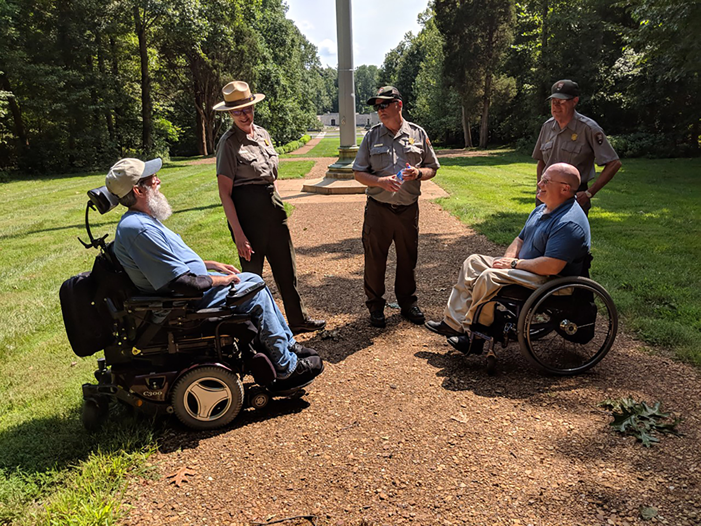 Two men in wheelchairs meet with Park Rangers on park trail.
