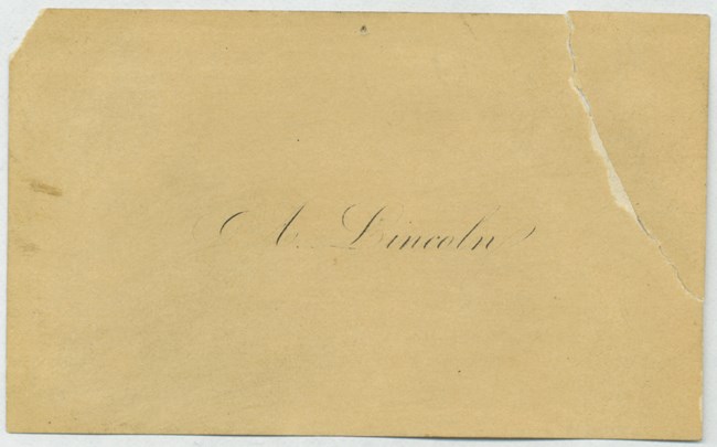 a paper card with a tear in the upper right corner and faded with age, about the size of a business card. "A. Lincoln" is printed on the card in faded, fancy script