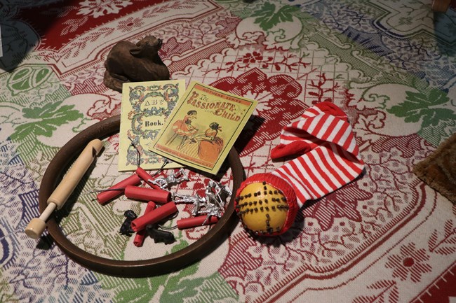 Assortment of small gifts including toy soldiers, firecrackers, whistle, tiny books, wooden toy, and a orange studded with cloves in a stocking