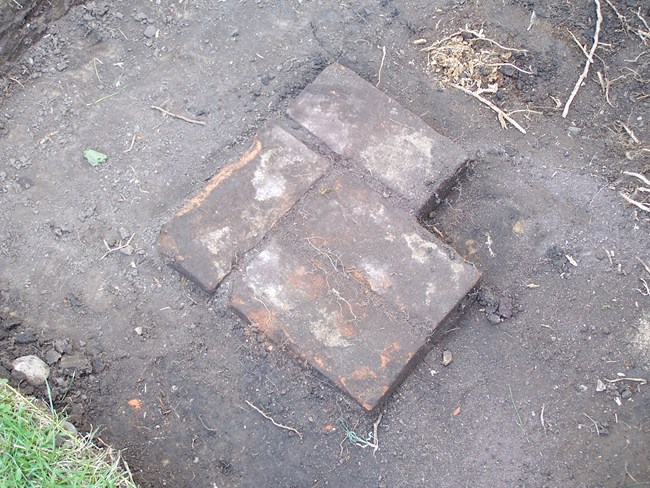 Dark brown soil lightly covers red brick, revealed during an archeological dig.