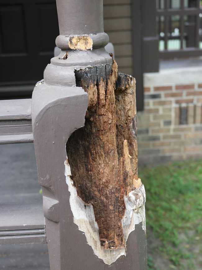 A wooden porch column, painted brown, with significant termite damage.