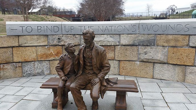 Bronze statue of Abraham Lincoln with son on lap in front of curved stone wall