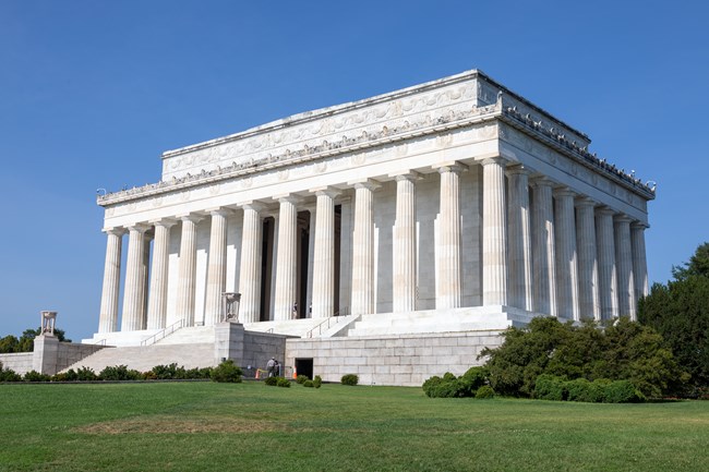 A series of wide steps lead up to a large rectangular marble building with columns.