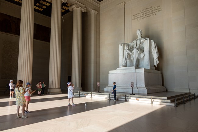 Visitors take pictures in front of a large marble statue of President Lincoln