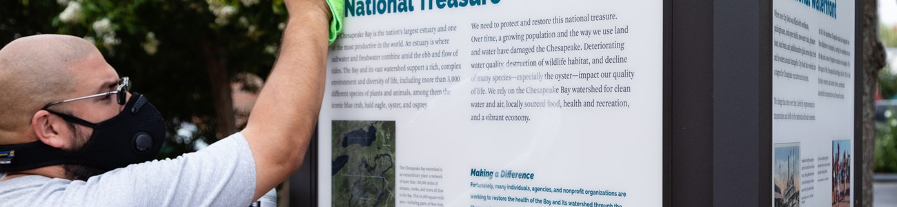 A man wipes down an interpretive sign titled "National Treasure."