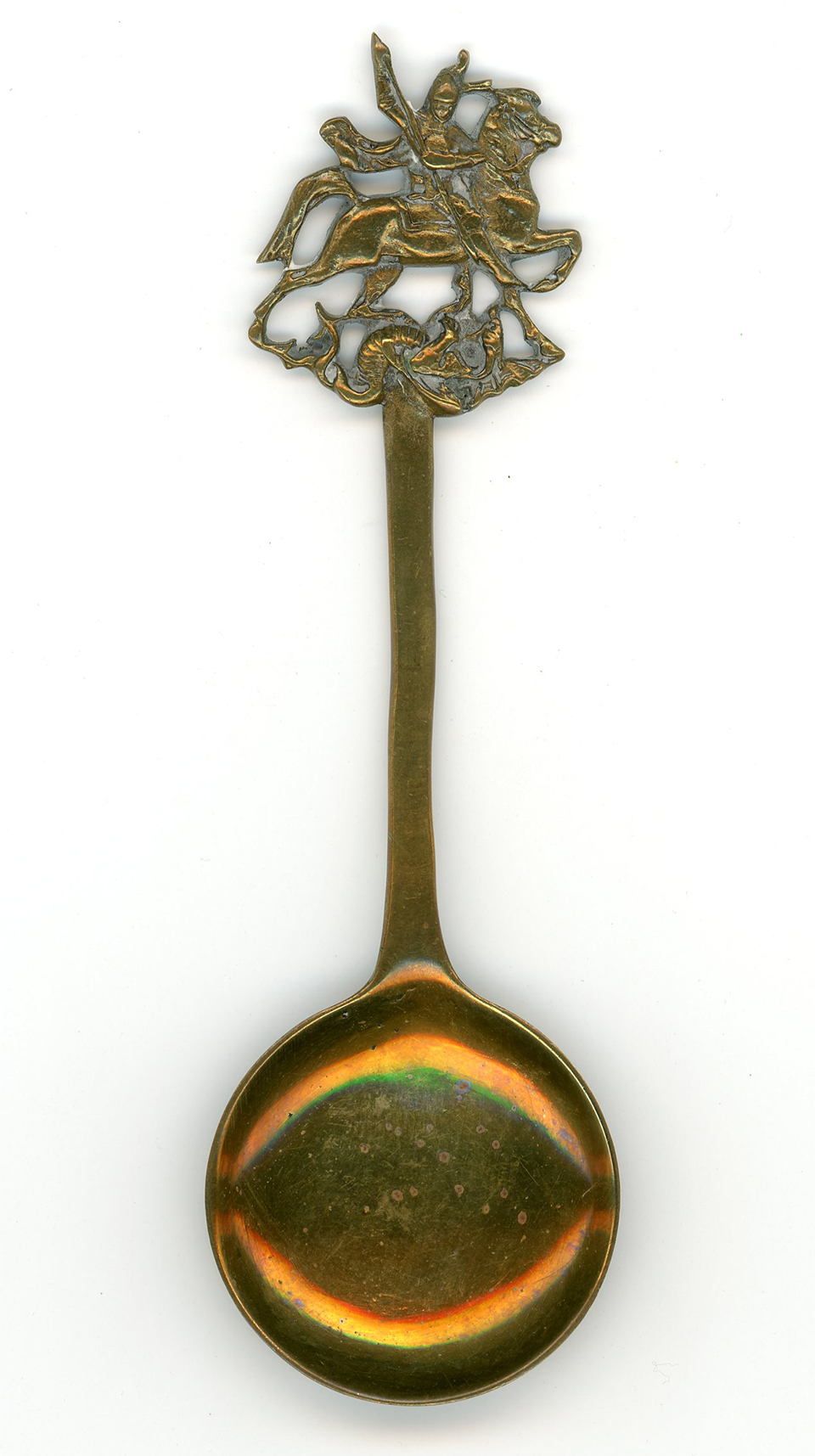 A brass spoon with circular bowl and an image of St. George slaying the dragon on the end of the handle.
