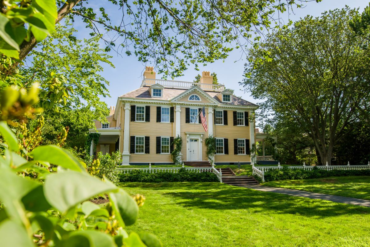 Front facade of yellow Georgian house, with greenery in foreground