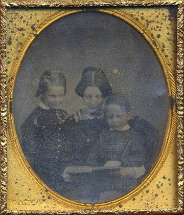 Daguerreotype of woman reading to two boys in oval case opening.