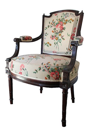 Armchair with seat and back upholstered in floral pattern on tan background.