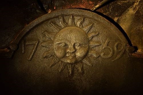 Iron fireback depicting a sun with a face flanked by the date 1759