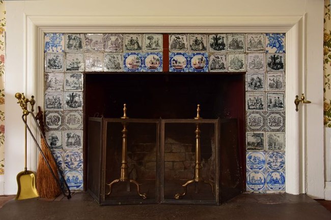 Fireplace with andirons and screen surrounded by multicolored tiles