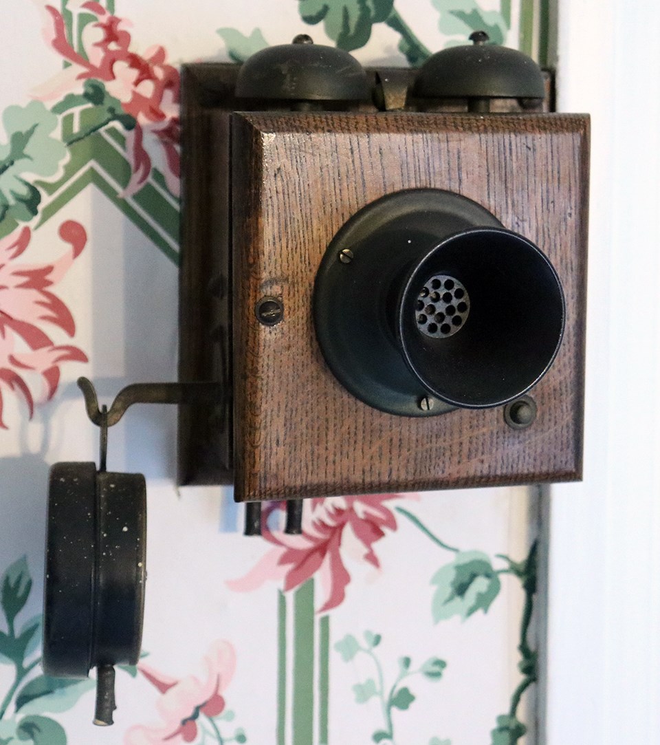 An early 20th century intercom system incorporating a wall-mounted wooden box with bells, a receiver, and a separate earpiece.