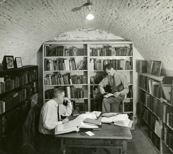 Two men surrounded by books in the basement archives, circa 1935