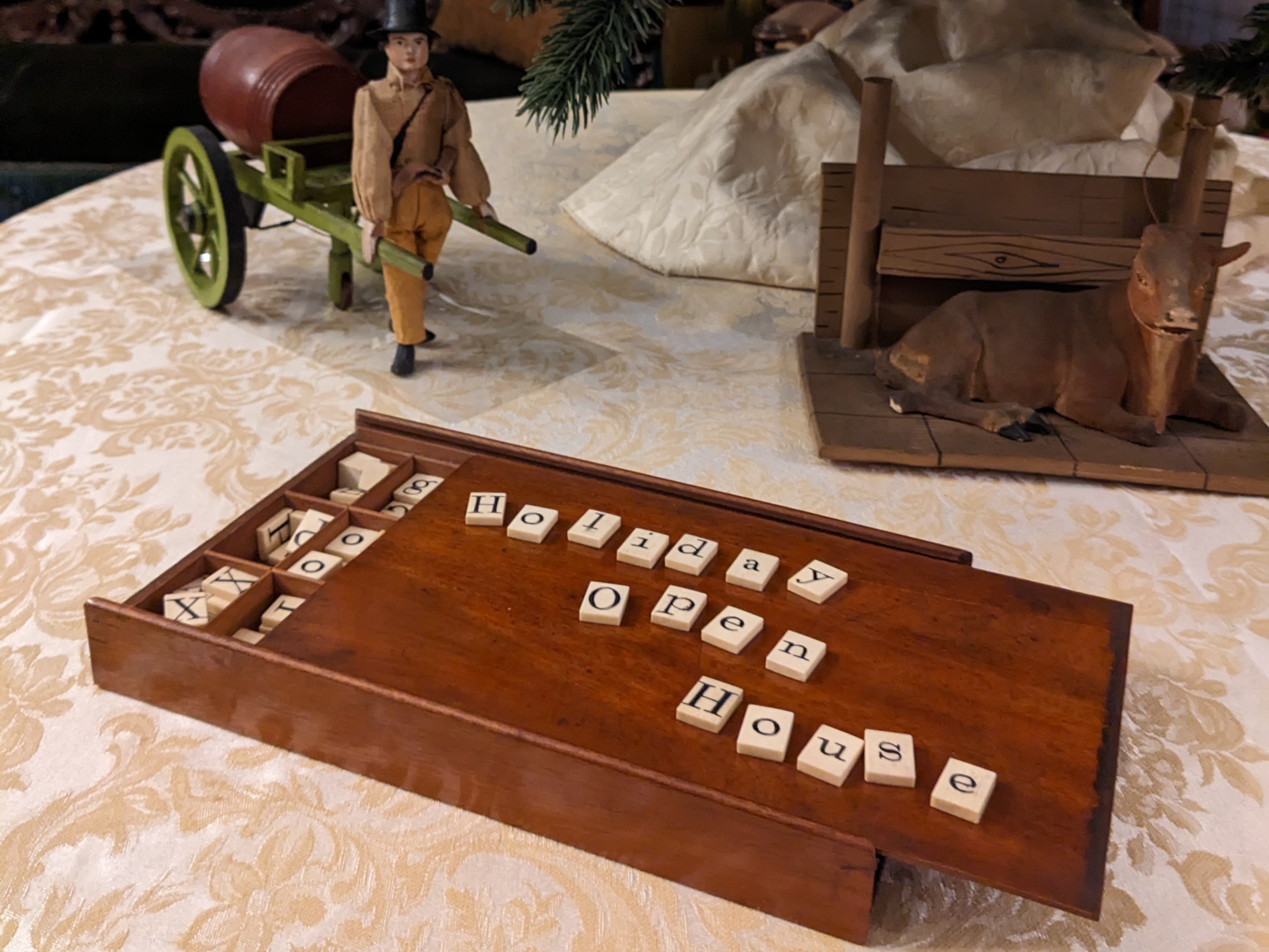 19th century game board showing "Holiday open house" in letter tiles with toys and tree in background