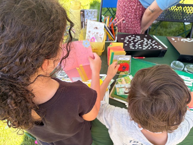 Two children explore an activity table with crafts and nature cards