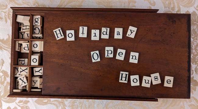 Tiles from a 19th century word game spell out "Holiday Open House" on top of a wooden box