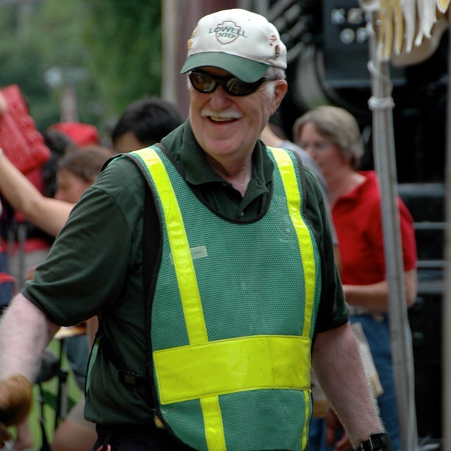 A park volunteer wearing a safety vest walks next to a trolley