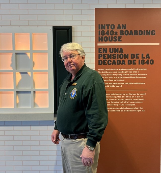 Man in National Park Service polo stands outside of an exhibit titled "Into an 1840s Boarding House"