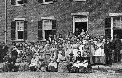 A long brick boardinghouse with workers posed outside