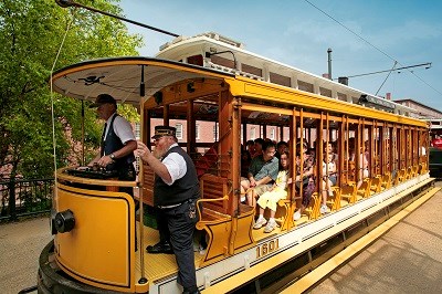 A green and yellow trolley full of visitors travels past a historic mill building