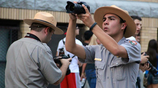 A park ranger holding a camera taking a picture while another park ranger takes a picture with his back towards us.