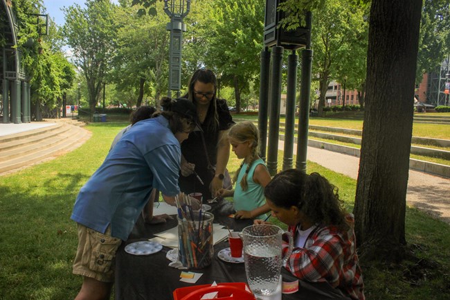 Visitors and staff gather around a table full of art supplies