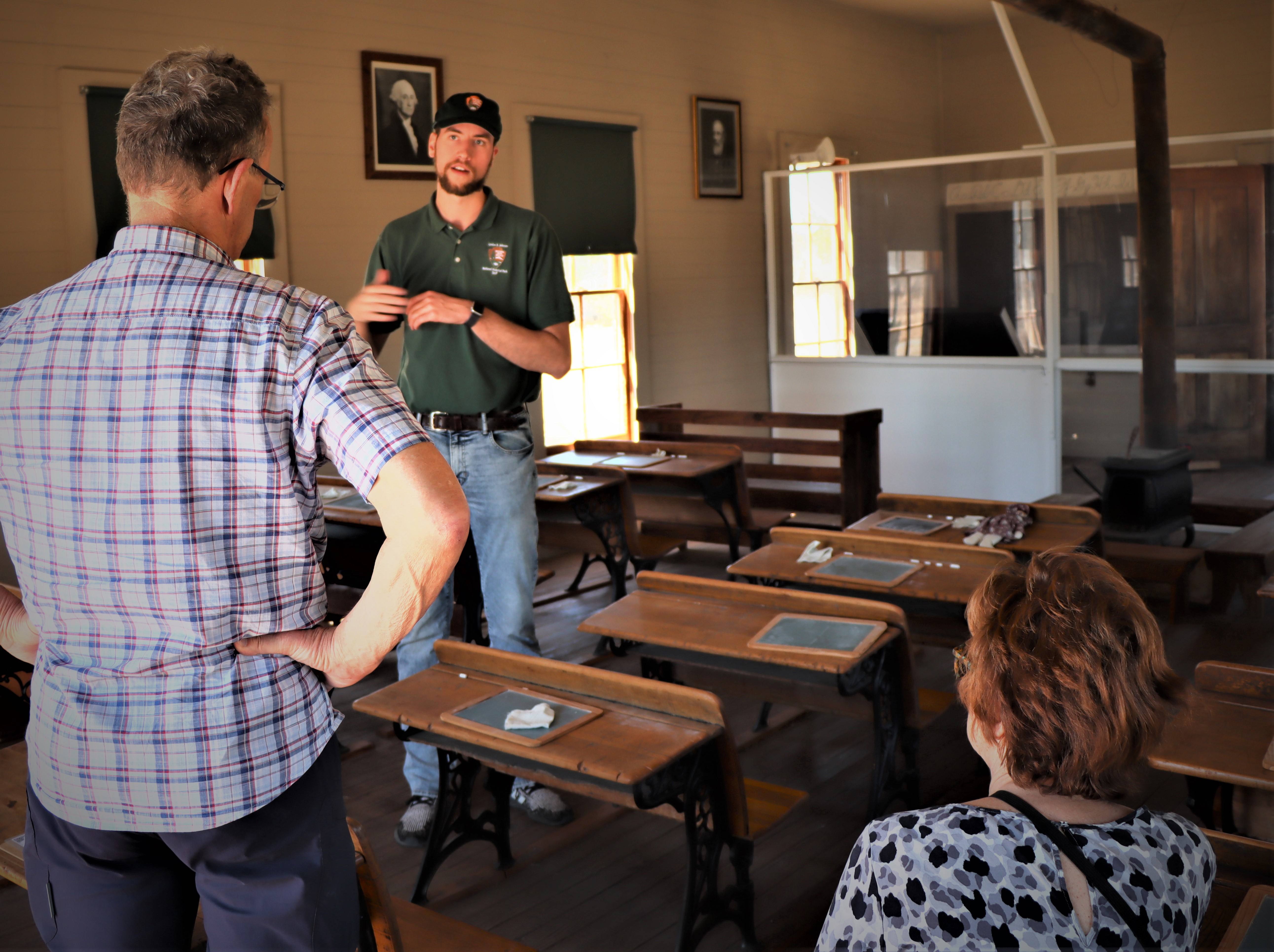 A tall young man talks with visitors about the one-room Junction School they are standing in.