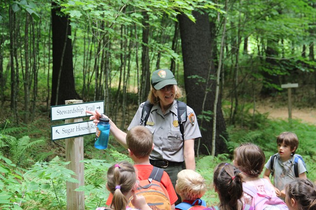 park ranger with kids on a trail points at sign