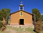 A pinkish-brown adobe chapel stands against the deep blue New Mexican sky.