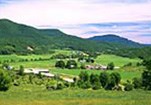 An aerial scene of farm buildings and green pastures nestled in Vermont’s forested hills.