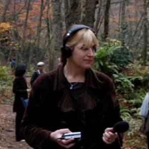woman stands in forest with microphone and headphones