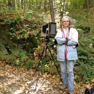 Woman stands next to camera on tripod in forest