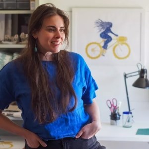 person in blue shirt stands with hands in pockets and artwork in background