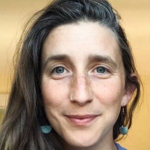 close headshot of woman wearing blue earrings and blue shirt