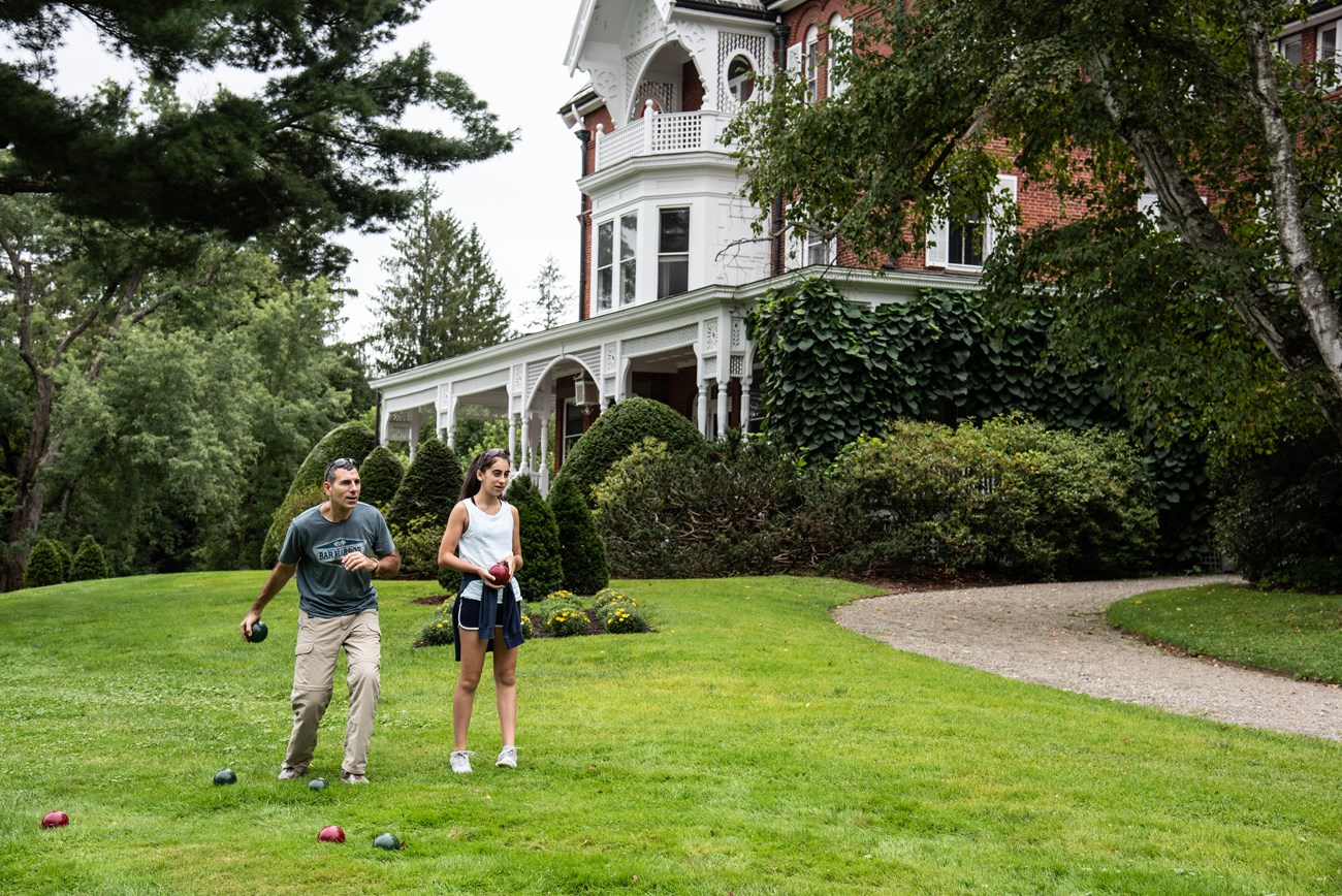Two park visitors in casual clothes play bocce ball in front of Marsh-Billings-Rockefeller mansion
