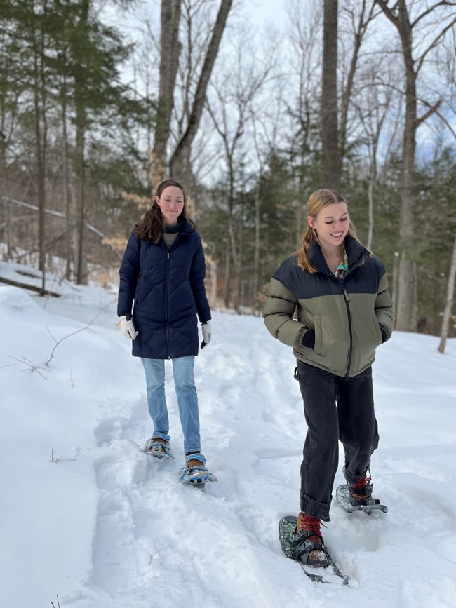 two people snowshoe on trail in forest