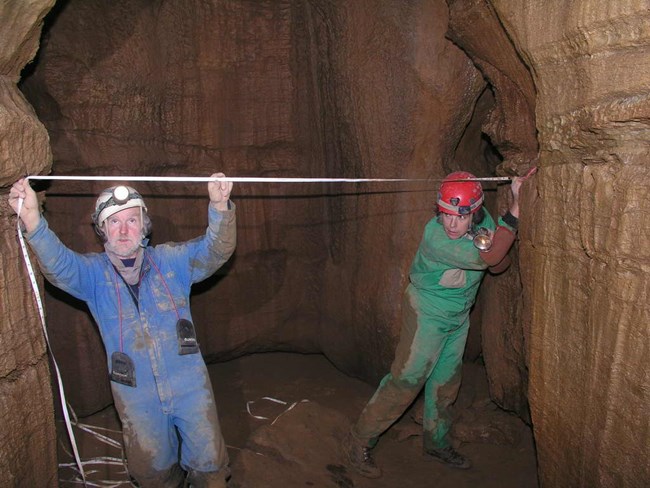 Two people use a tape measure to measure the cave width.