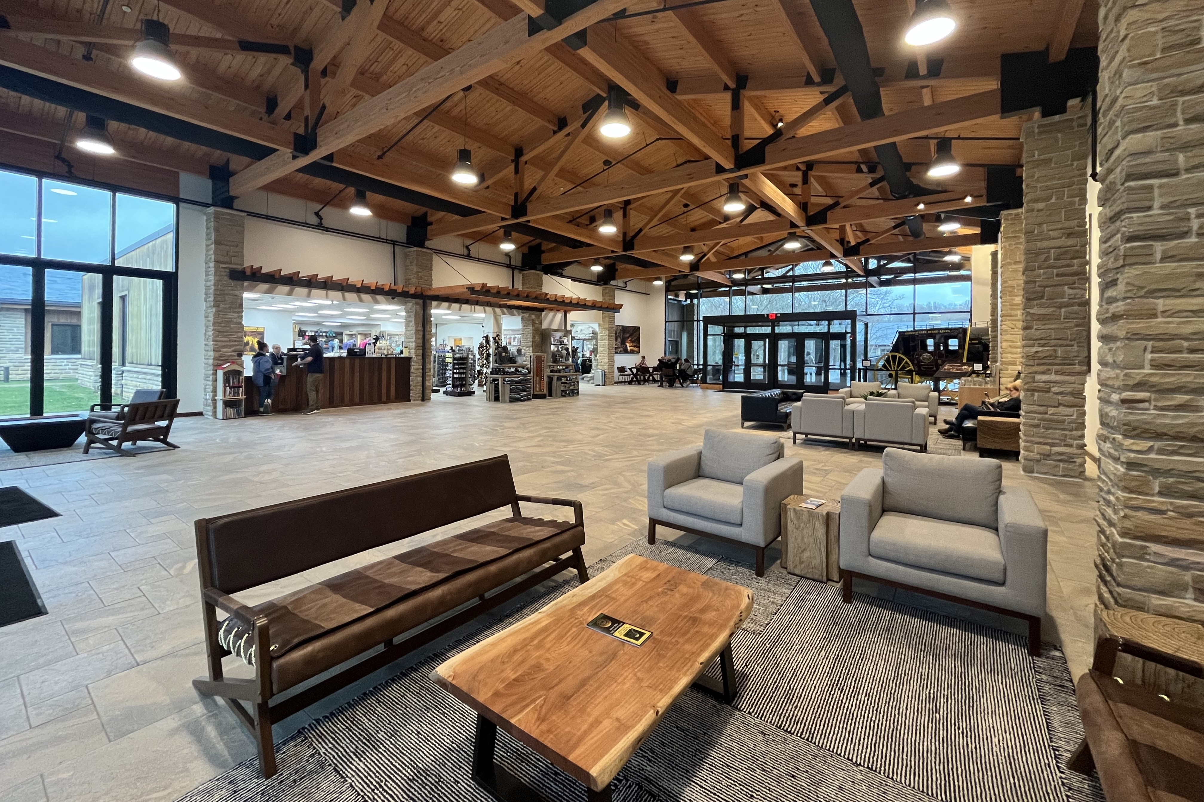 A large room with wooden beams, stone columns, and scattered furniture in neutral colors.