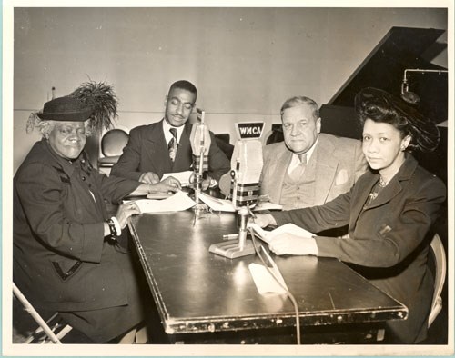 Four figures sit at a table with microphones