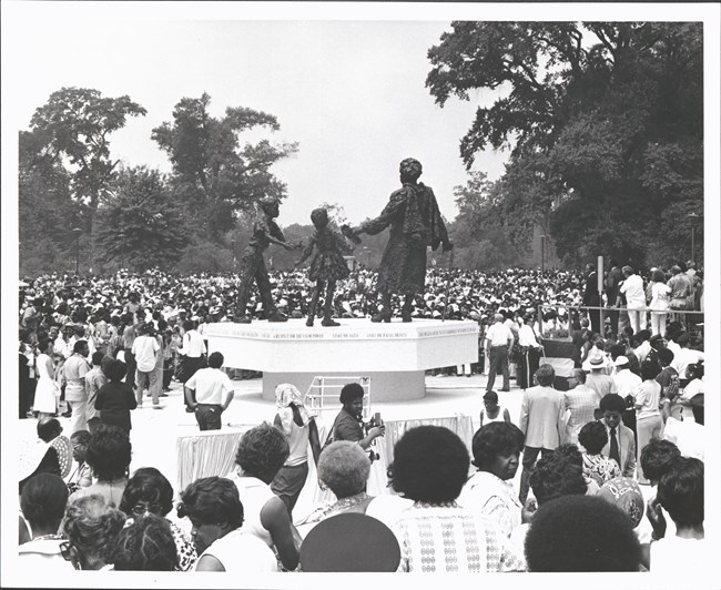 A large crowd gathers outside at a monument