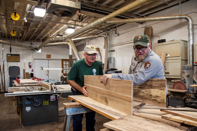 An NPS employee and a volunteer fit a piece of wood onto a coffin