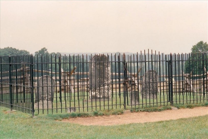 A modern color photo of three gravestones surrounded by a black iron fence.